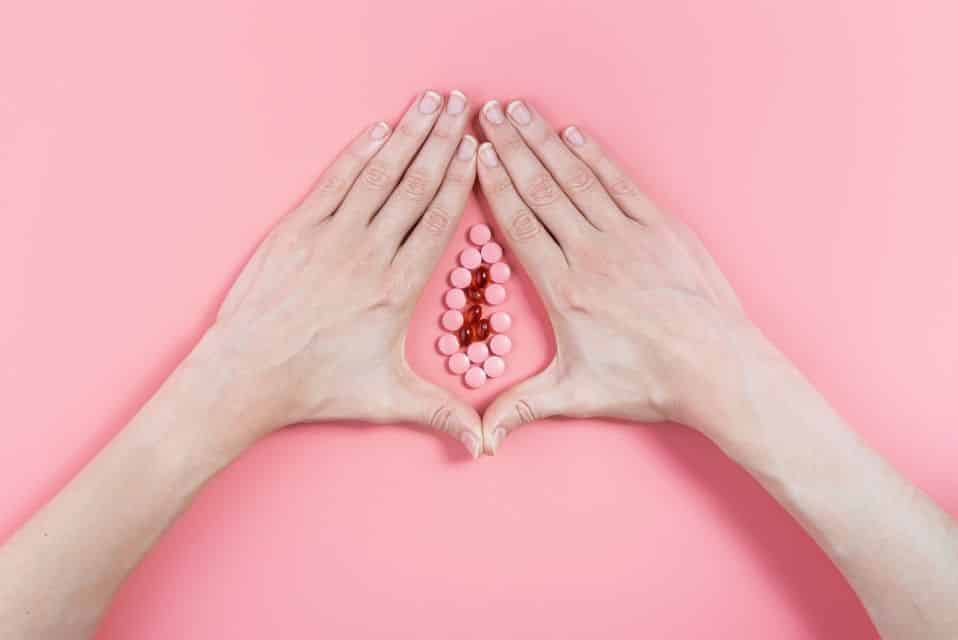 Imagem abstrata de uma vagina feita com as mãos e desenho com pilulas para corrimento esbranquiçado