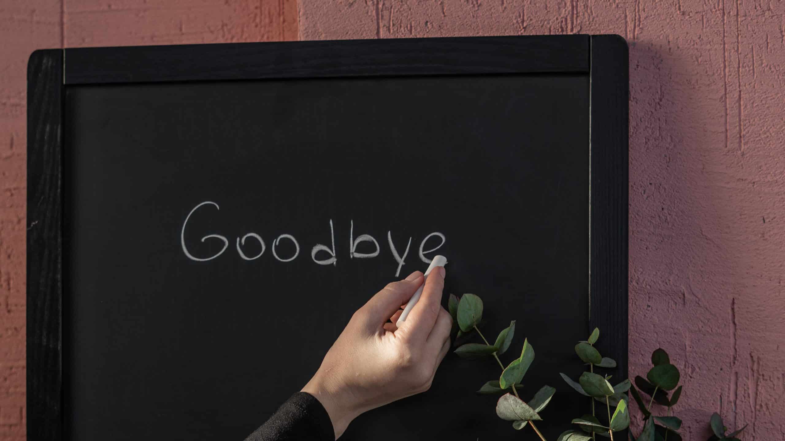 Mão escrevendo a palavra "goodbye" (adeus) em um quadro
